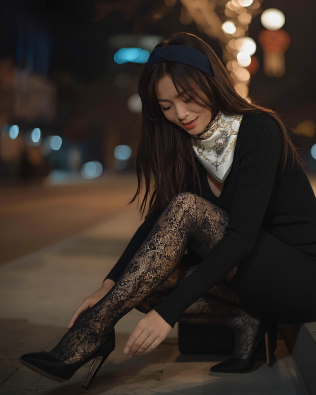 Woman adjusting her high-heeled shoes on a street at night.