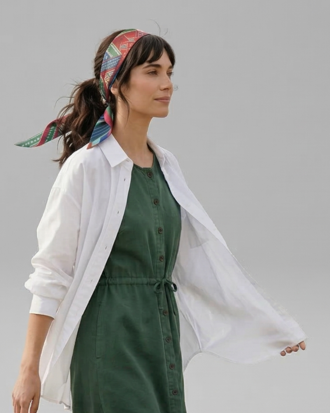 Woman wearing a green dress with a white oversized shirt and colorful headscarf on a gray background