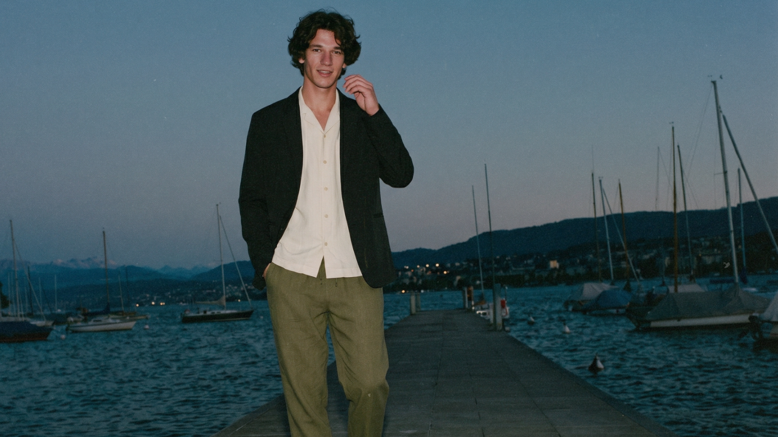 Man standing on a dock with boats and mountains in the background