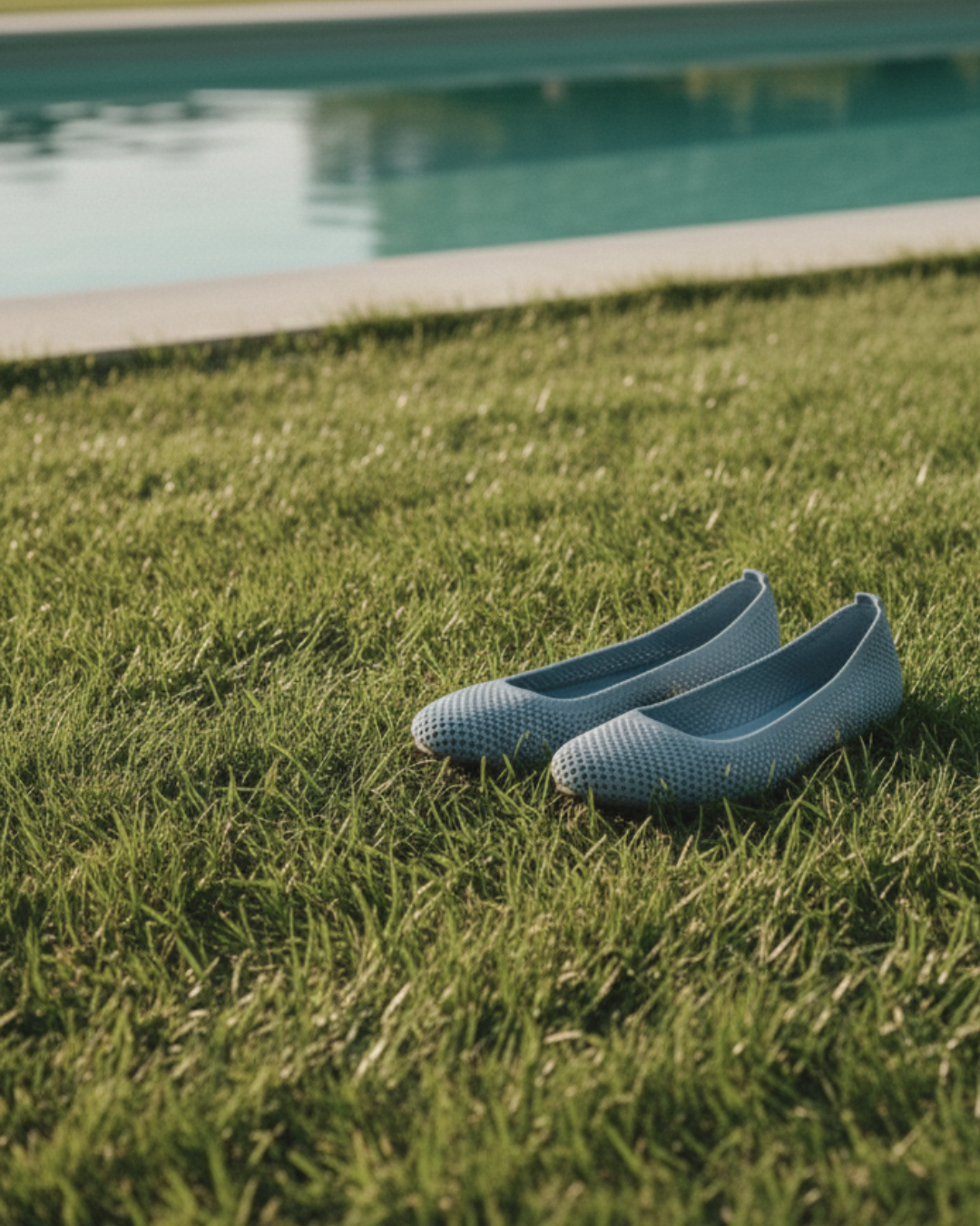 Pair of light blue textured shoes on green grass with a pool in the background