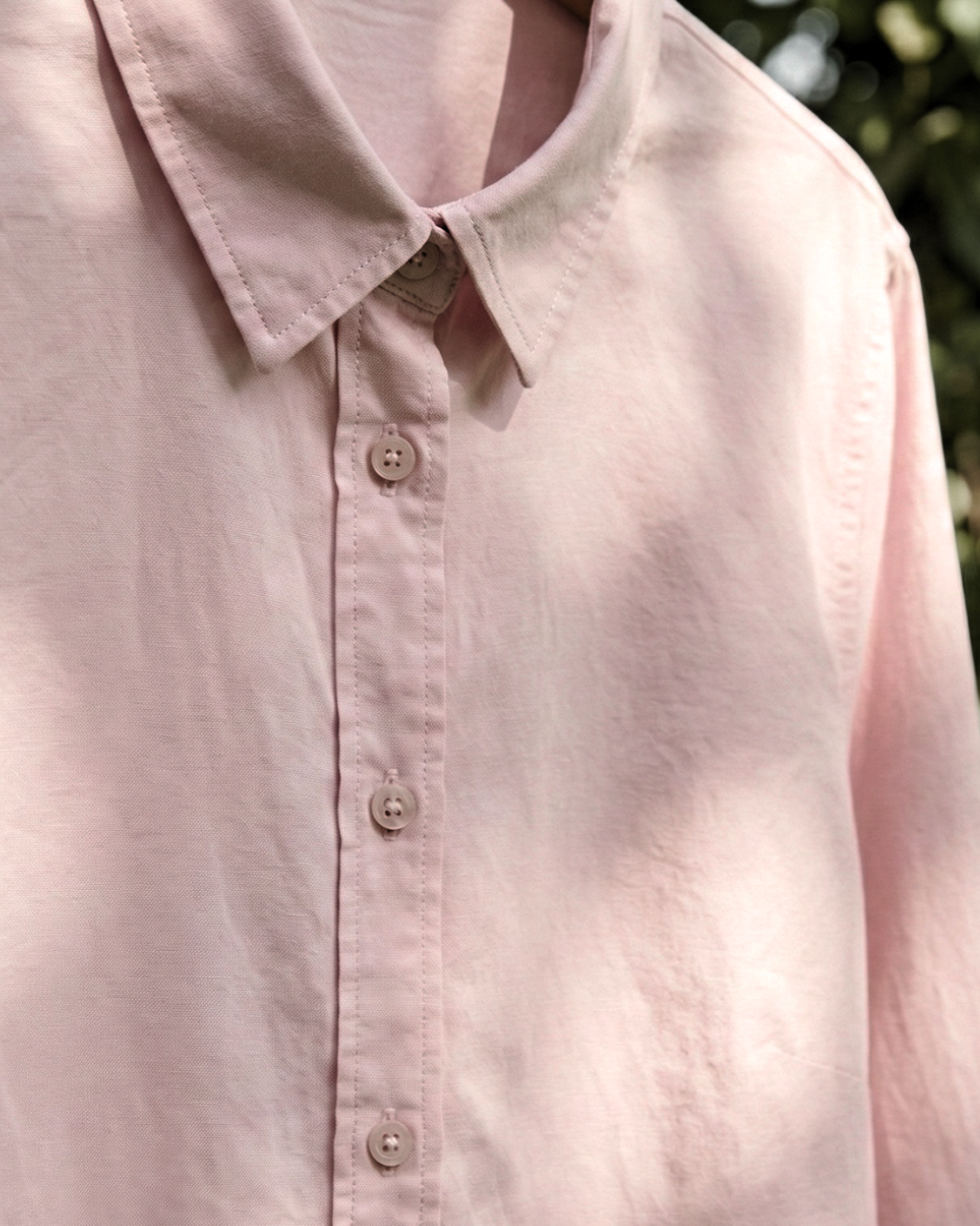 Close-up of a light pink shirt with buttons against a blurred natural background